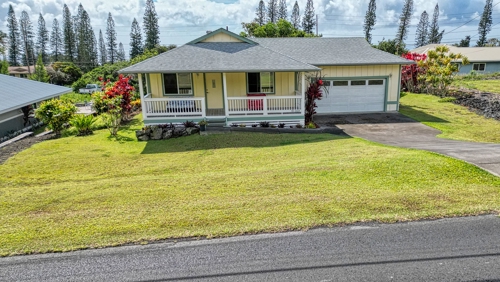 This charming home features a classic front porch, a well-kept lawn, and a freshly maintained exterior. The attached garage and paved driveway add convenience, while the surrounding tropical landscaping enhances its curb appeal.