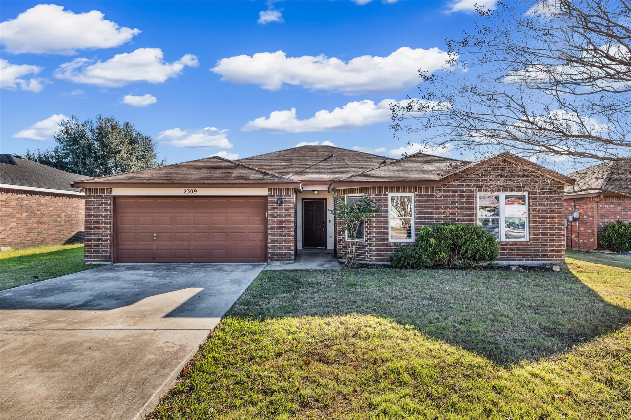 Front view of home with driveway, brick siding, a front lawn, and an attached garage
