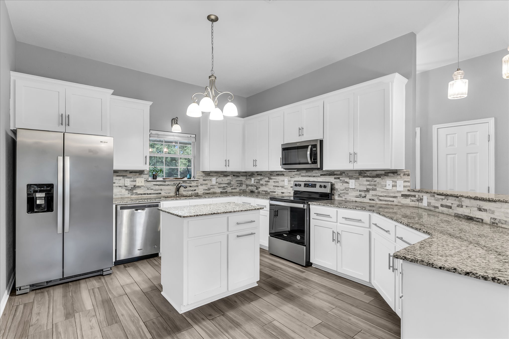 Open-concept kitchen featuring white cabinetry, stainless steel appliances, a multi-tone tile backsplash, light speckled countertops, and wood-finish flooring